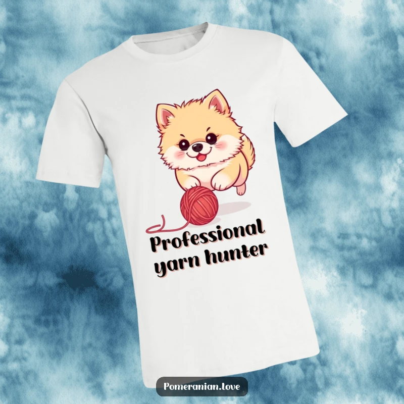 Funny Pomeranian t-shirt depicting a cute dog with intense focus, playfully chasing a rolling ball of yarn. Ideal for dog lovers.